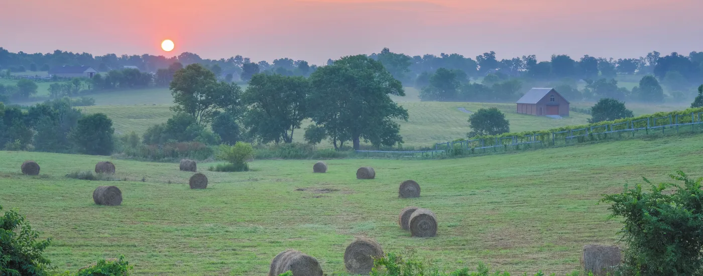 Sunset in background with field and hay bales in the foreground