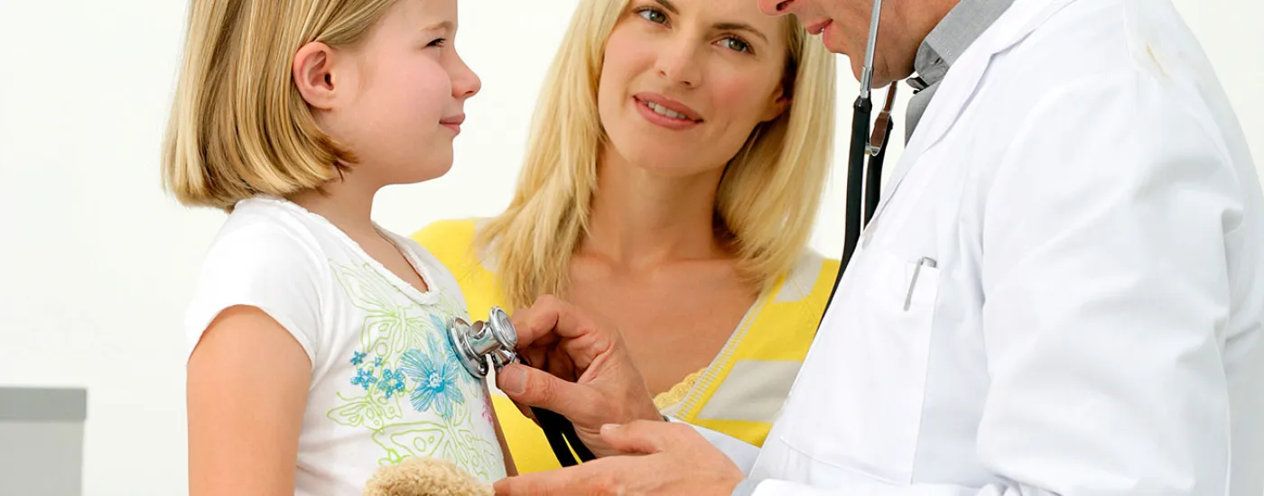 doctor listening to child's heart with stethoscope; parent standing in between