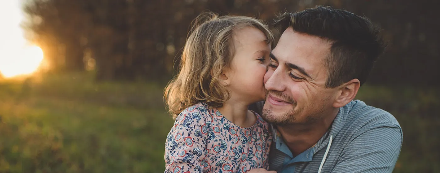 kid kissing parent on cheek in field